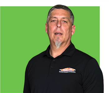 Man sitting at a desk wearing a black and green SERVPRO shirt smiling