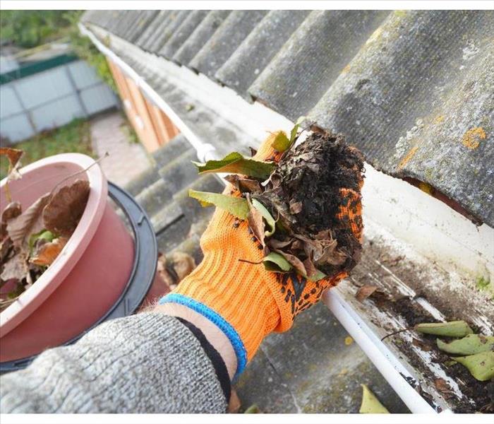 Hand with a glove cleaning a dirty gutter